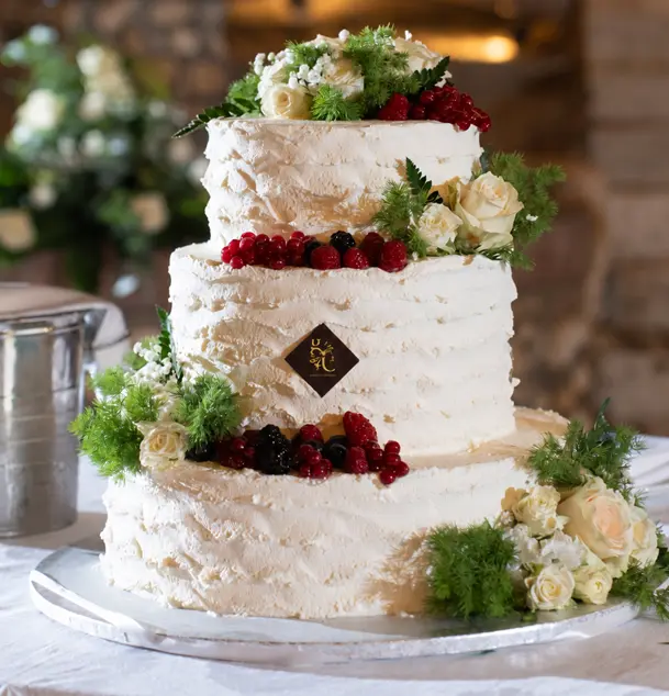 Torta artigianale a tre piani decorata con rose bianche, frutti rossi e dettagli verdi